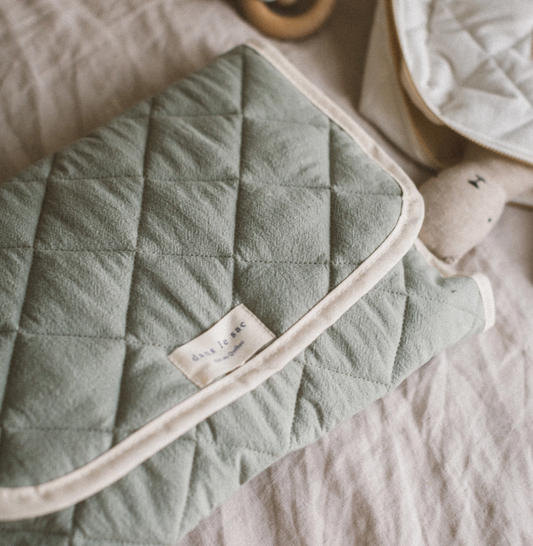 A folded green cotton quilted baby changing mat with a visible brand label, 100% cotton, made in Quebec, Canada.