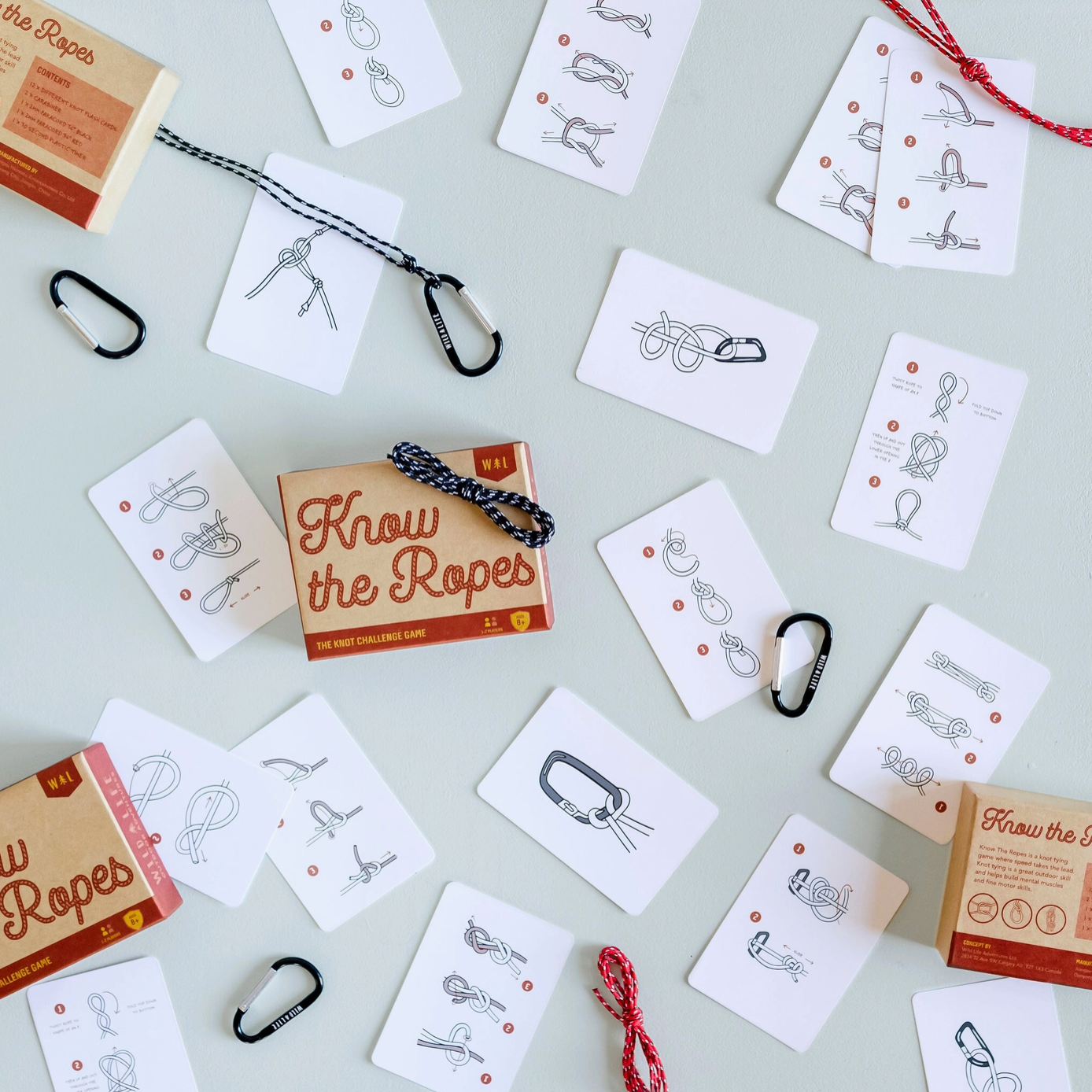 The image shows the 'Know the Ropes' knot challenge game spread out with various knot flash cards, carabiners, and pieces of paracord.